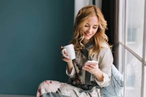 pretty blonde girl sitting window sill with cup